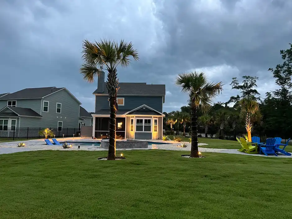 Backyard at dusk with a lit pool, palms wrapped in lights and chairs on the lawn