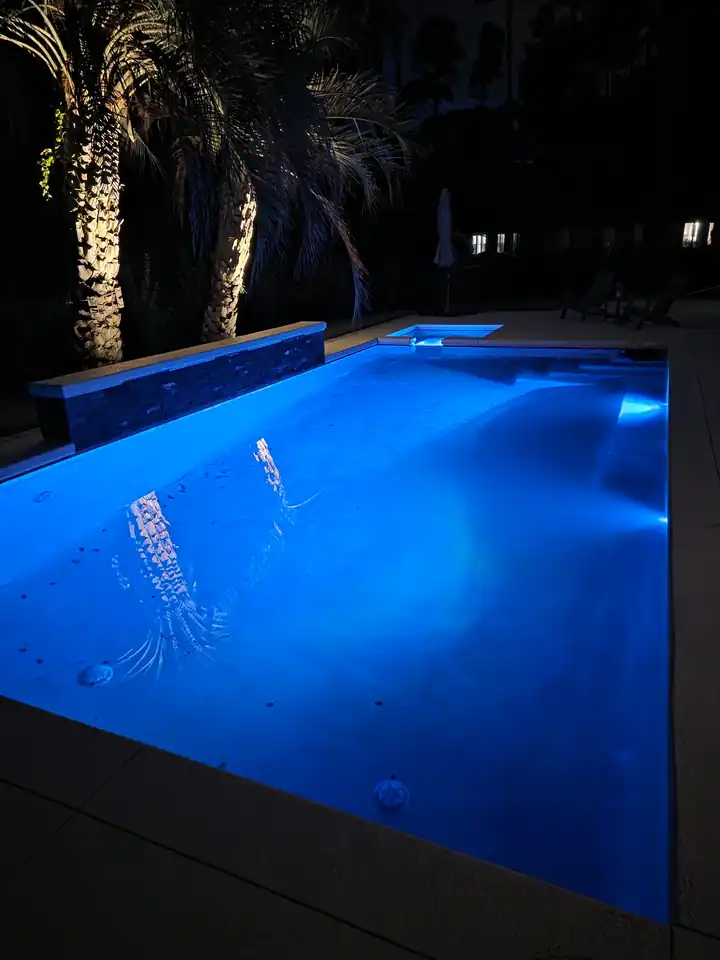Pool lit blue at night with a waterfall spill and palms