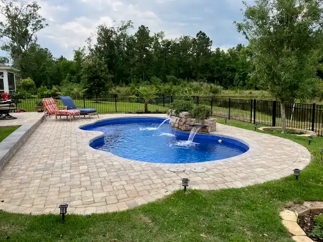 Freeform fiberglass pool with a paver deck and a small rock waterfall