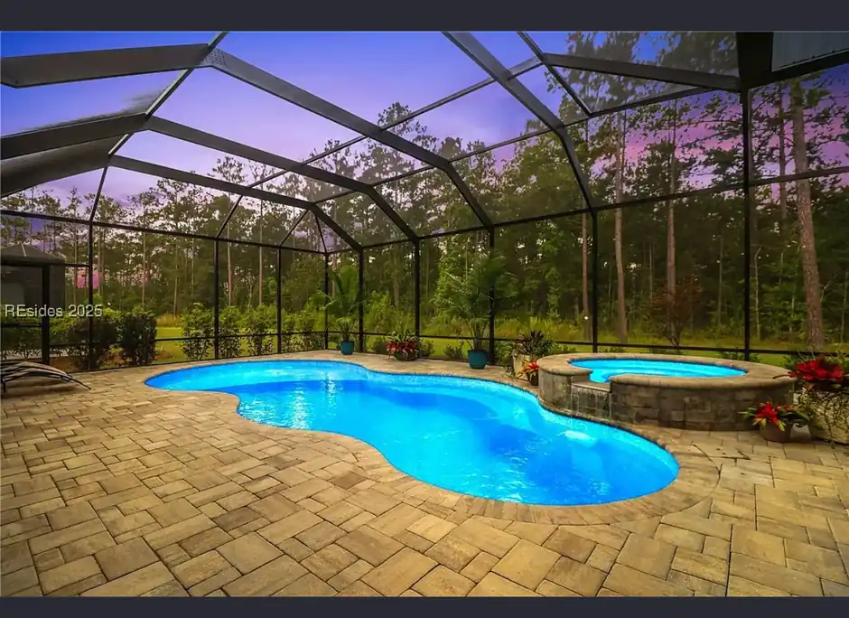 Screened lanai with a pool and spa at dusk and a brick-paver deck