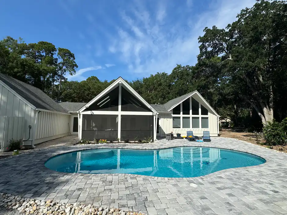 Freeform pool ringed by grey pavers in front of a gabled screened porch