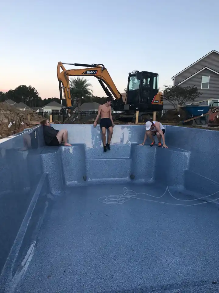 A new pool shell in a cleared backyard with an excavator parked behind it