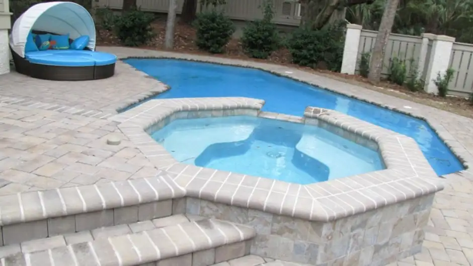 Angular pool with an attached spa and a canopy daybed on a paver deck