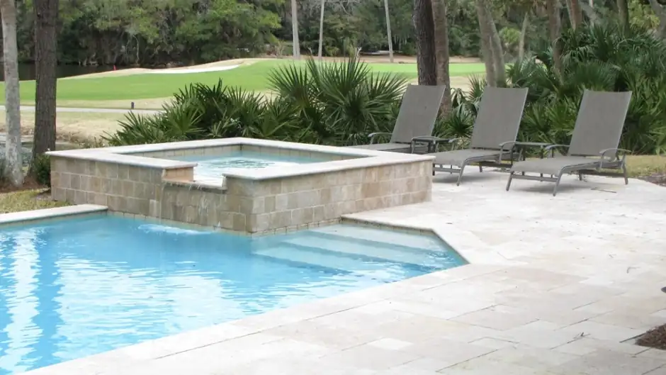 Travertine pool deck with a raised stone spa and loungers beside a golf course