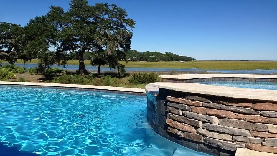Raised stacked-stone spa wall spilling into a pool with marsh grass beyond