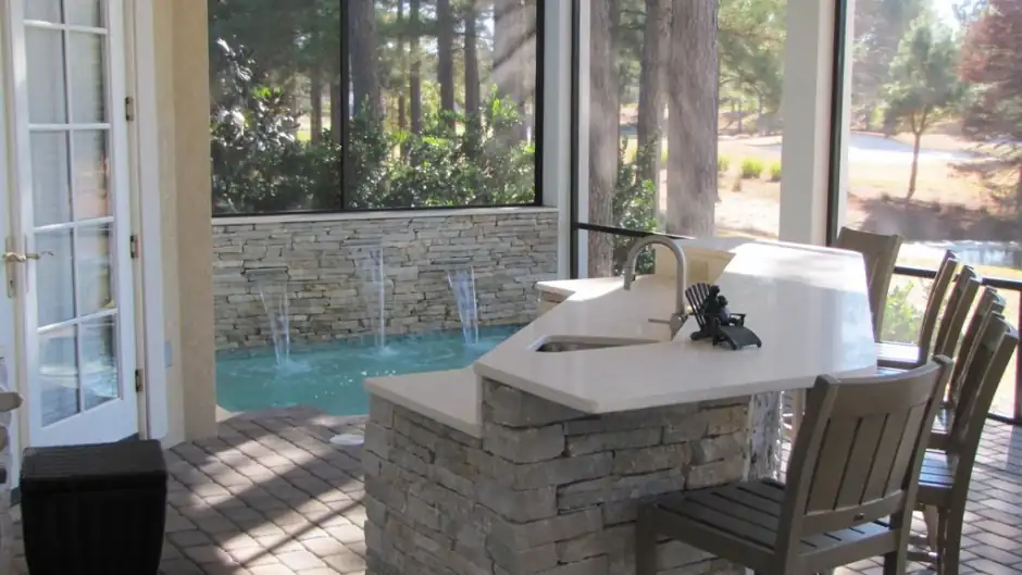 Stacked-stone wall with a sheer water descent into a pool beside a screened kitchen