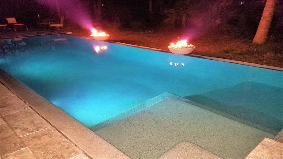 Pool at night lit from below with two fire bowls burning on its edge